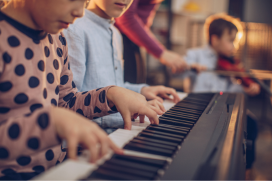Kind speelt op keyboard. Op de achtergrond meer kinderen met muziekinstrumenten.