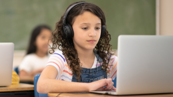 Kind zit achter laptop in klaslokaal met koptelefoon op het hoofd